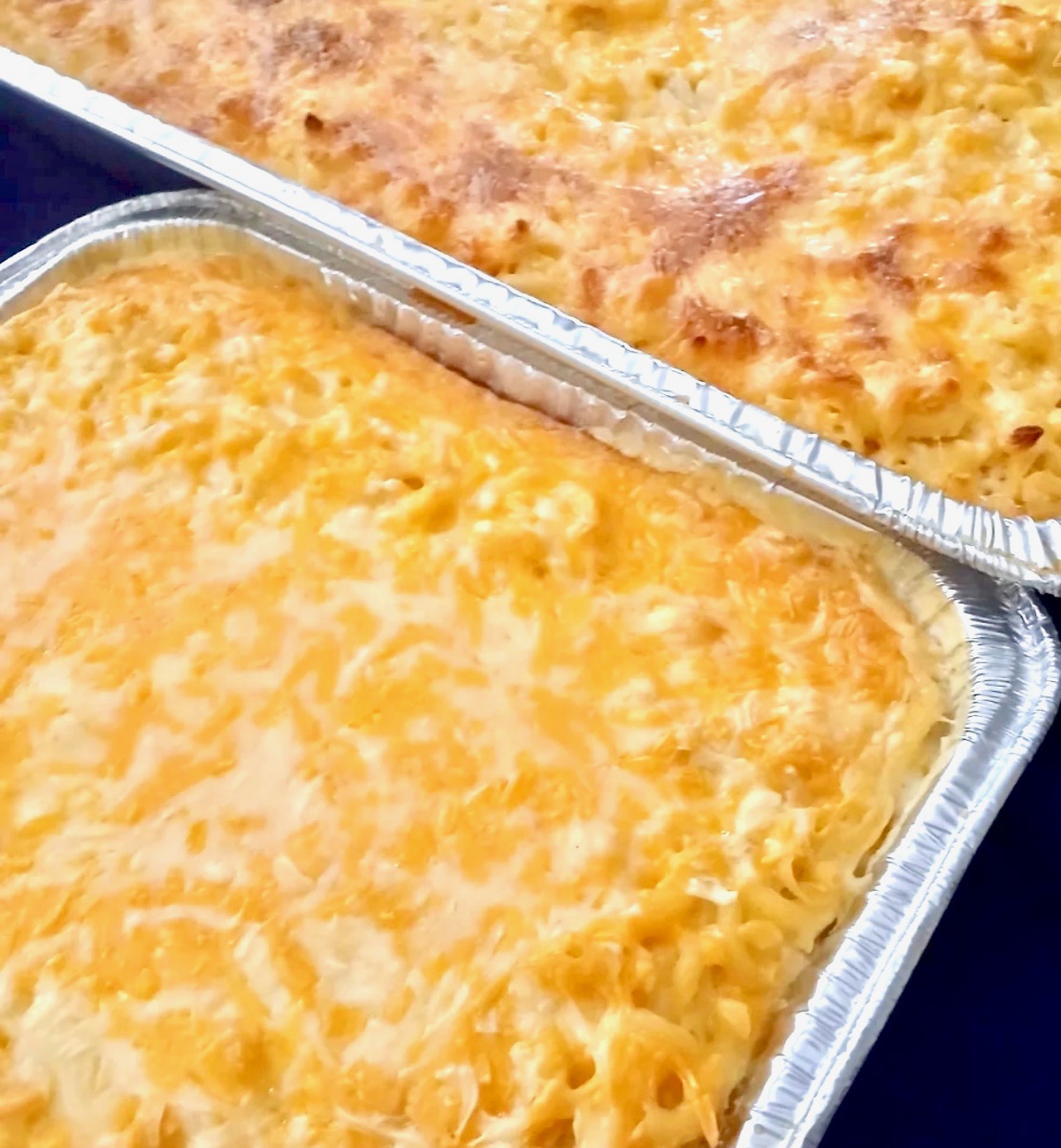 Two pans of baked four cheese macaroni with golden bubbling cheese crust