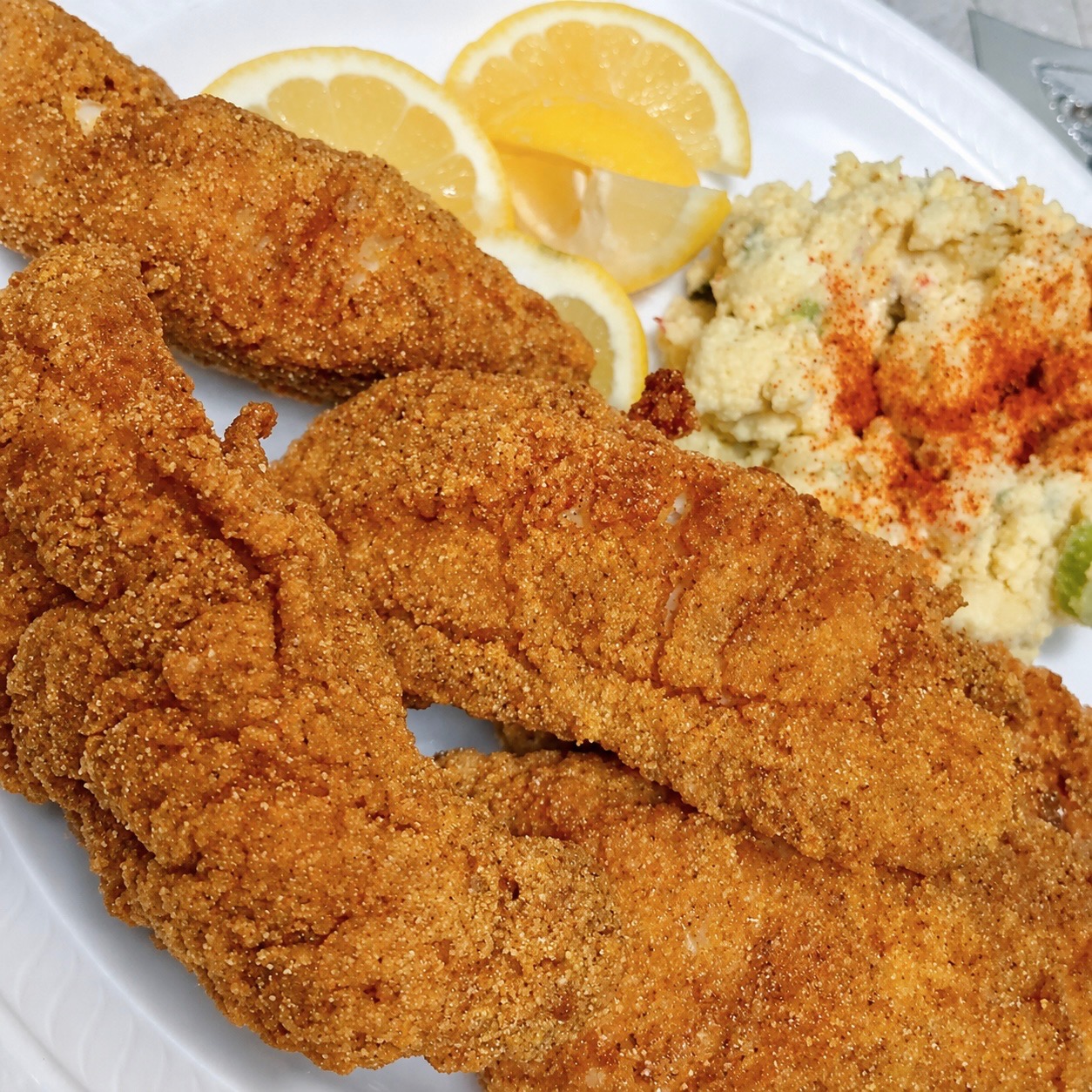 Golden cornmeal crusted fried catfish fillets plated with potato salad and fresh lemon